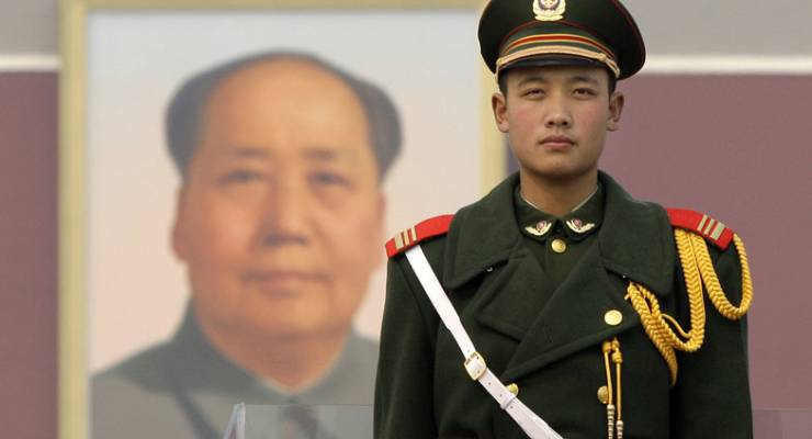 A Chinese soldier stands in front of a portrait of Mao