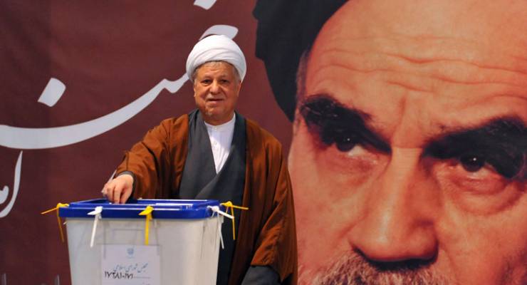 Former President Akbar Hashemi Rafsanjani casts his ballot for the parliamentary elections in front of a portrait of late Iranian leader Ayatollah Khomeini