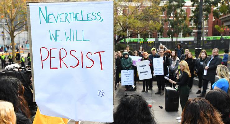Demonstraters at a rally hold a sign saying Nevertheless we will persist