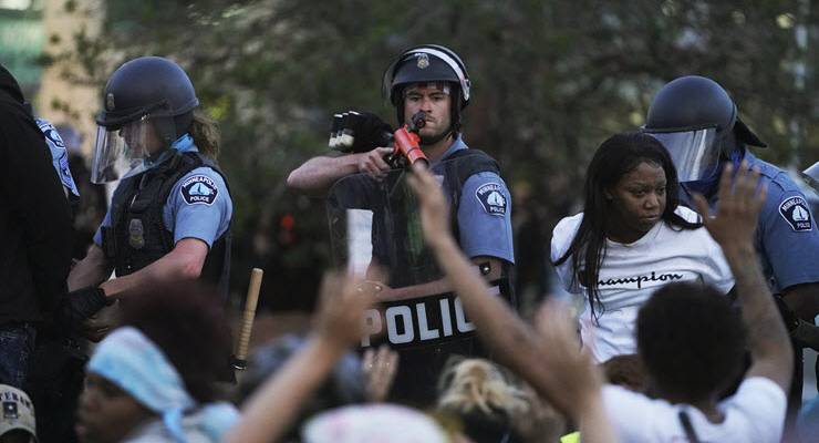 police officer aims weapon at protesters