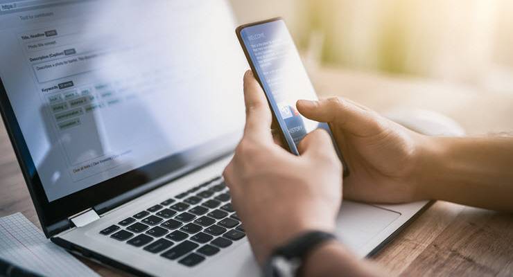 person texting on phone held over laptop