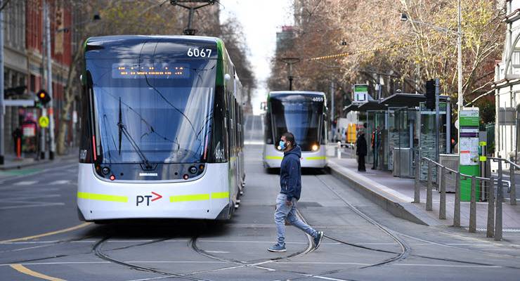 man wearing mask crossing tram tracks