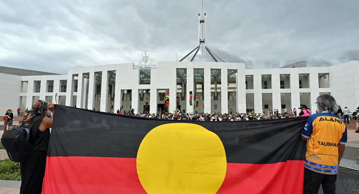Protesters hold the Aboriginal flag during a rally outside Parliament House (Image: AAP/Mick Tsikas)